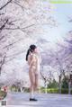 A woman in a white bikini standing in front of cherry blossoms.