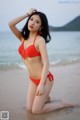 A woman in a red bikini sitting on the beach.