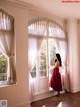 A woman in a red dress standing in front of a window.