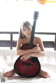 A woman sitting on a bed holding a guitar.